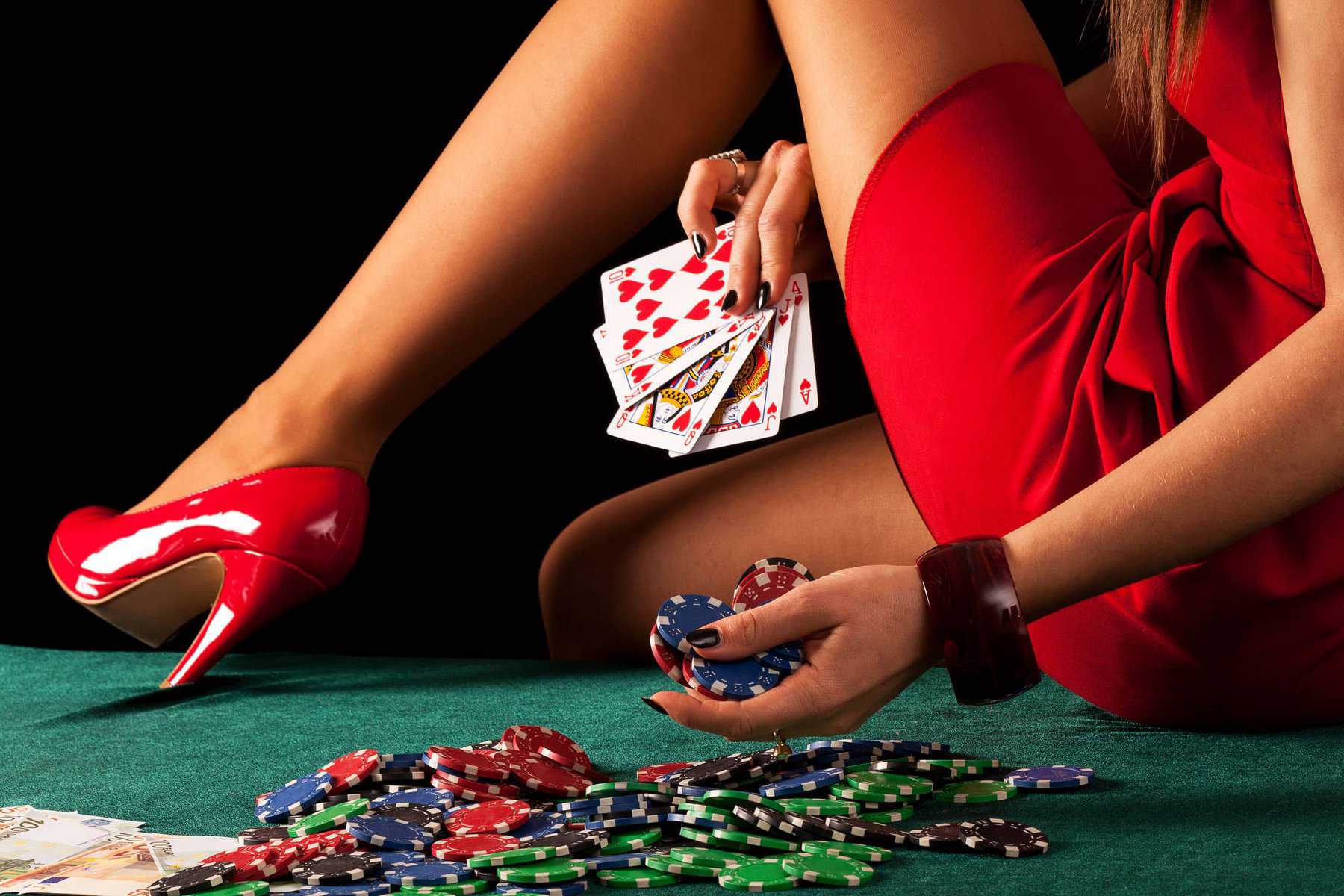 Una bailarina exótica en un vestido rojo sentada en una mesa con fichas de póker y cartas.
